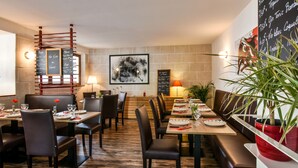A restaurant with wooden flooring, black leather chairs, and tables set with plates and glasses. There are chalkboards with menu items and a framed abstract painting on the wall. - Auberge L'Estanquet (Urt)