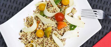 A white plate with quinoa salad, cherry tomatoes, and green peppers on a textured black surface.