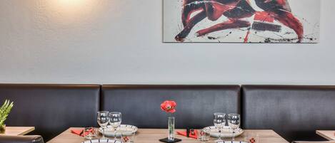 Un restaurante con una mesa lista para dos, un florero con una flor roja y una obra de arte colgada en la pared.