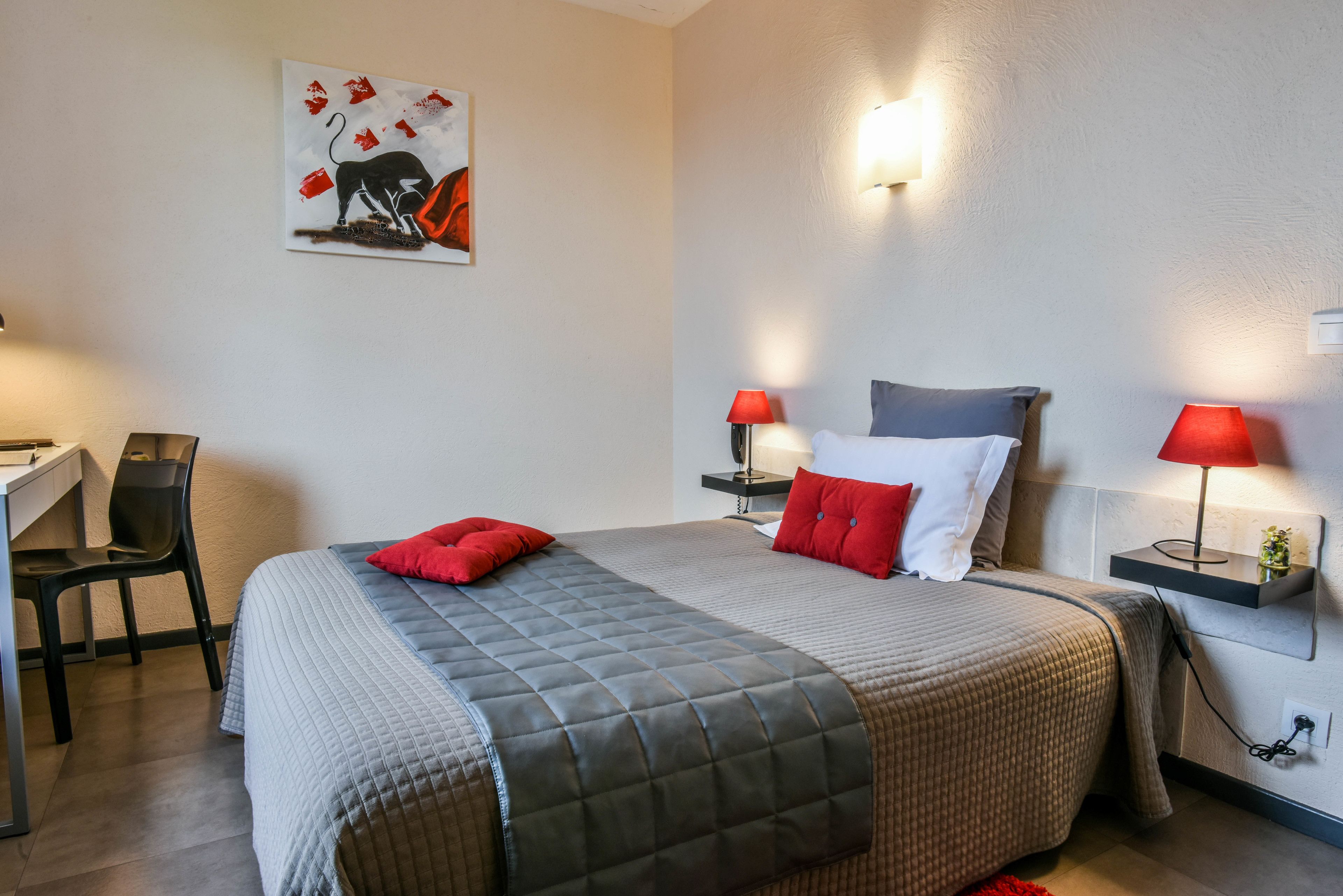 A hotel room with a bed, two bedside tables with lamps, a desk with a chair, and a wall-mounted artwork.