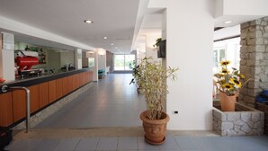 Um hall de hotel moderno com um balcão comprido, plantas em vasos e uma parede de pedra.