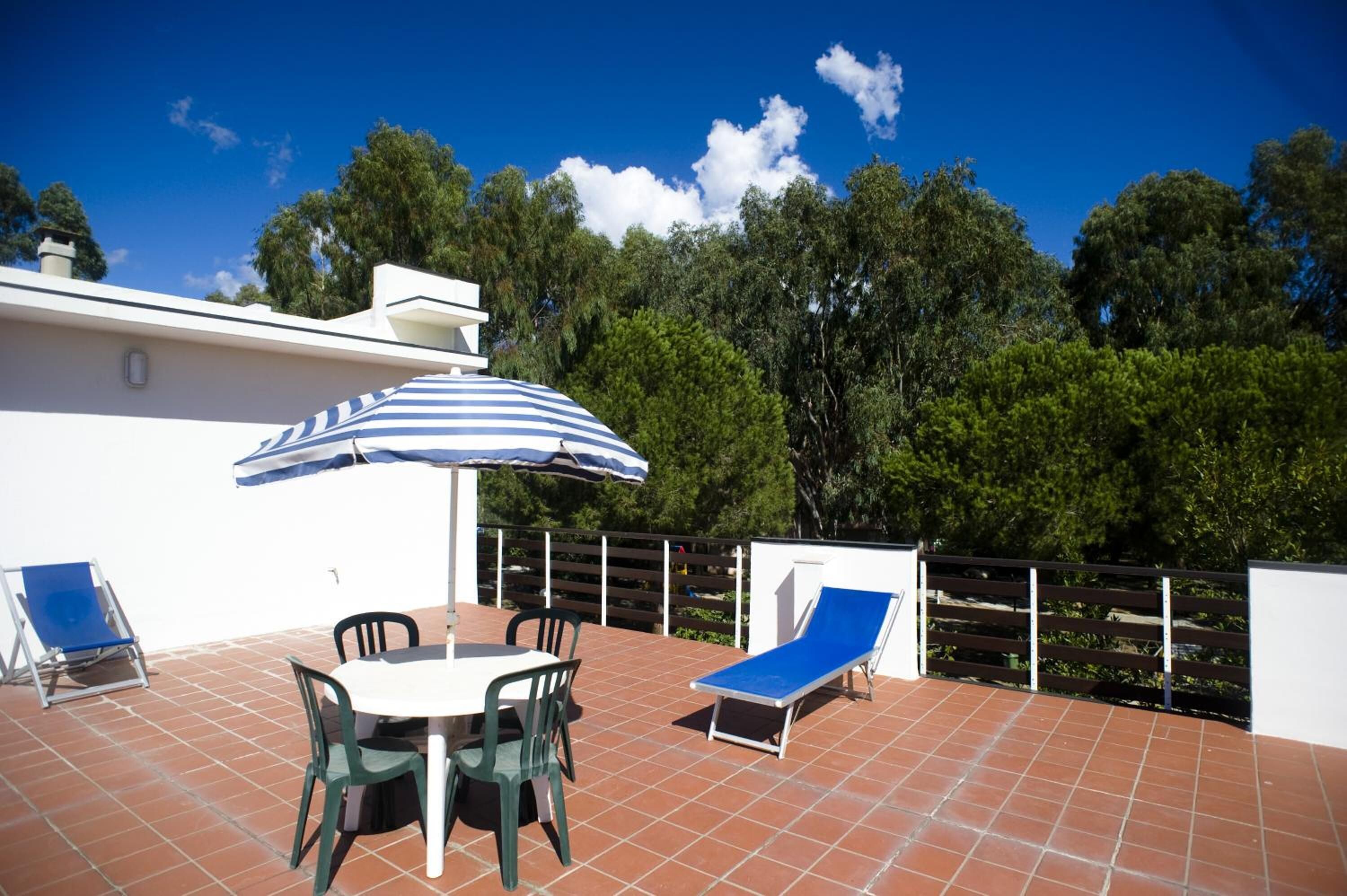 A patio with a table and chairs, a blue-striped umbrella, and two lounge chairs.