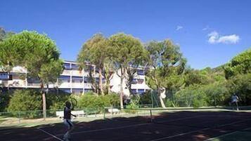 Una cancha de tenis con red, rodeada de árboles y un edificio al fondo.