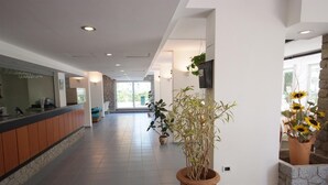 Um saguão de hotel com balcão de recepção, plantas em vasos e uma parede de pedra.