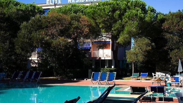 Piscina com espreguiçadeiras e guarda-sóis, cercada por árvores.