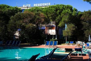 Ein Swimmingpool mit Liegestühlen und Sonnenschirmen, umgeben von Bäumen.