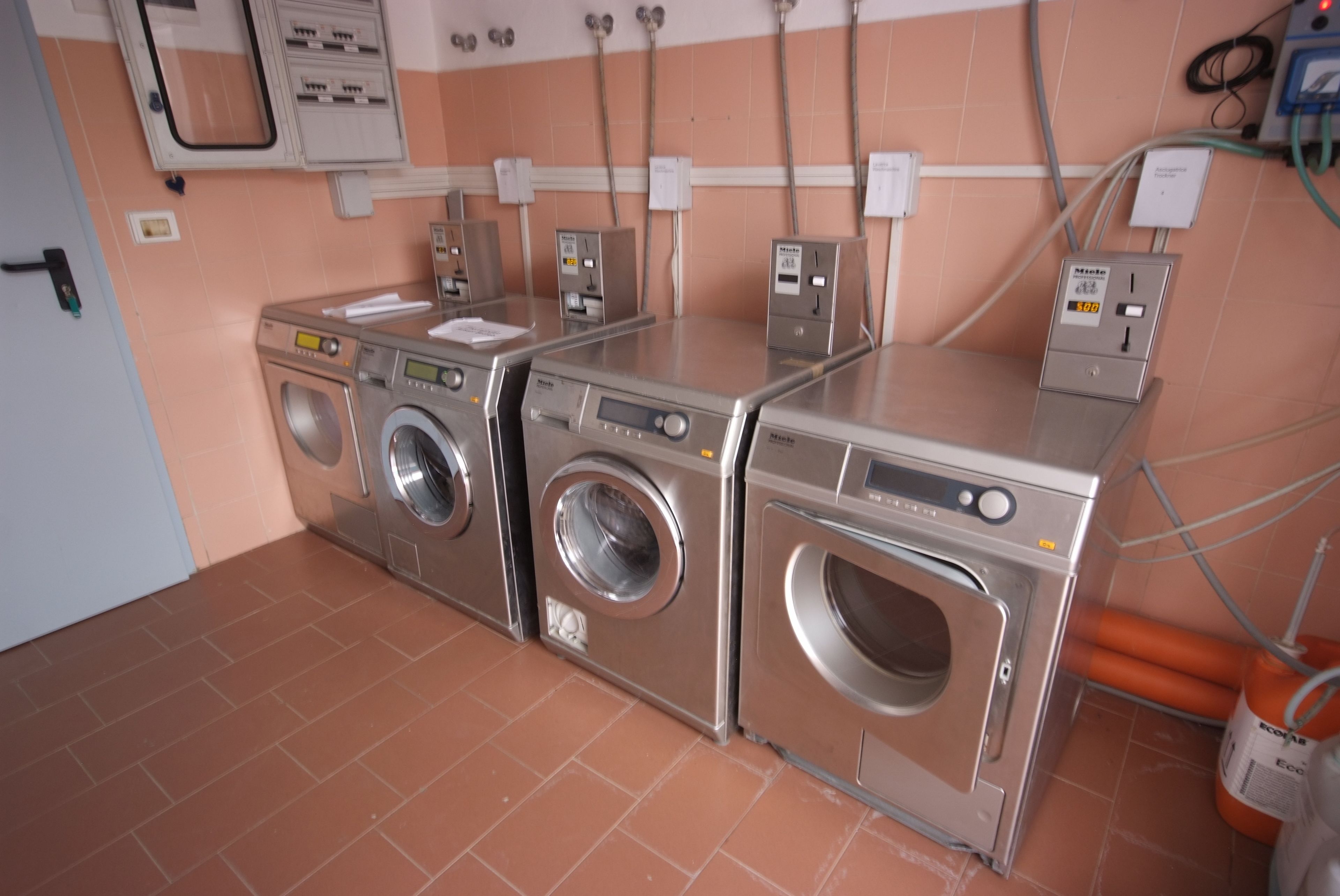 A laundry room with three stacked front-loading washing machines, a control panel, and a water heater.