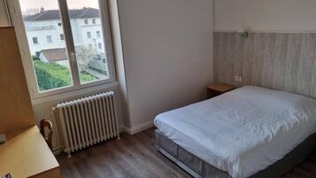 Un dormitorio con un ventanal grande, una cama, un radiador y un escritorio.