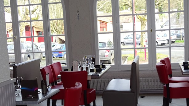 Restaurante com cadeiras vermelhas, uma mesa e vista para carros estacionados na rua.
