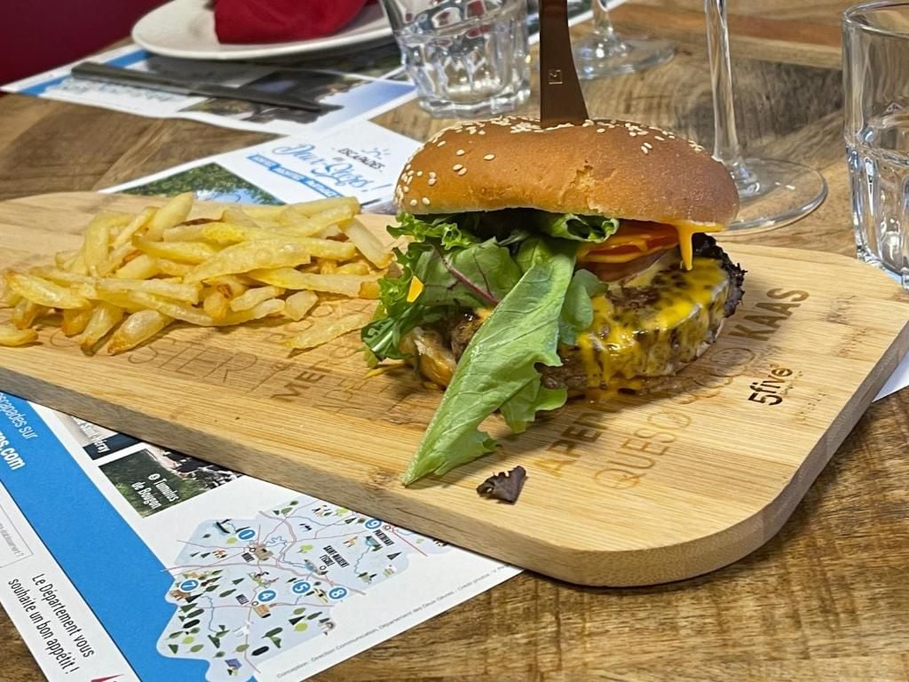 A burger with fries on a wooden board, a knife, and a glass of water on a table.