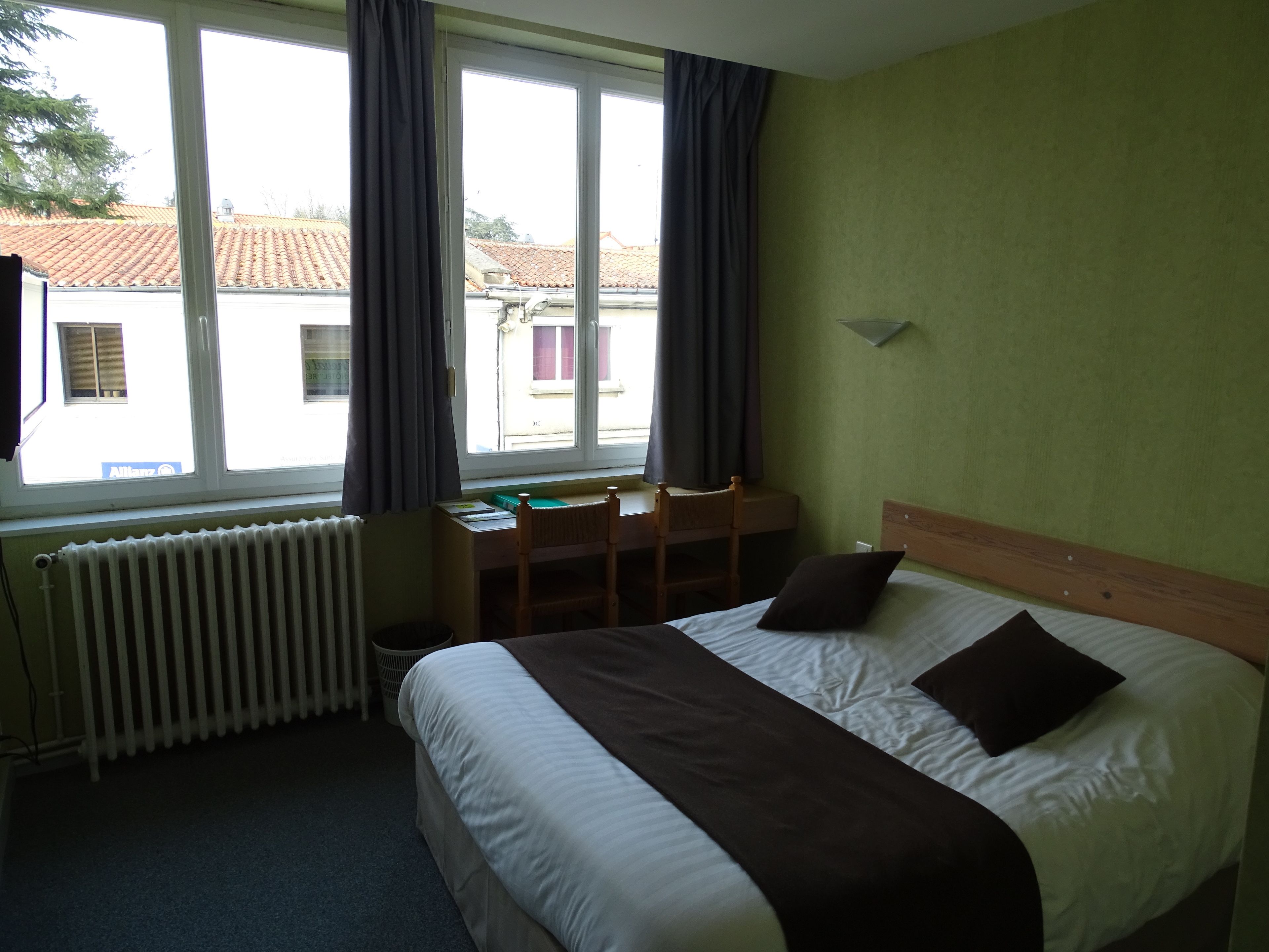 Una habitación de hotel con una cama, un escritorio y un ventanal con cortinas.