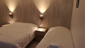 Quarto de hotel com duas camas, cada uma com mesa de cabeceira e luminária na parede.