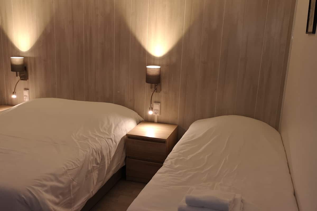 A hotel room with two beds, each with a nightstand and a wall-mounted lamp.