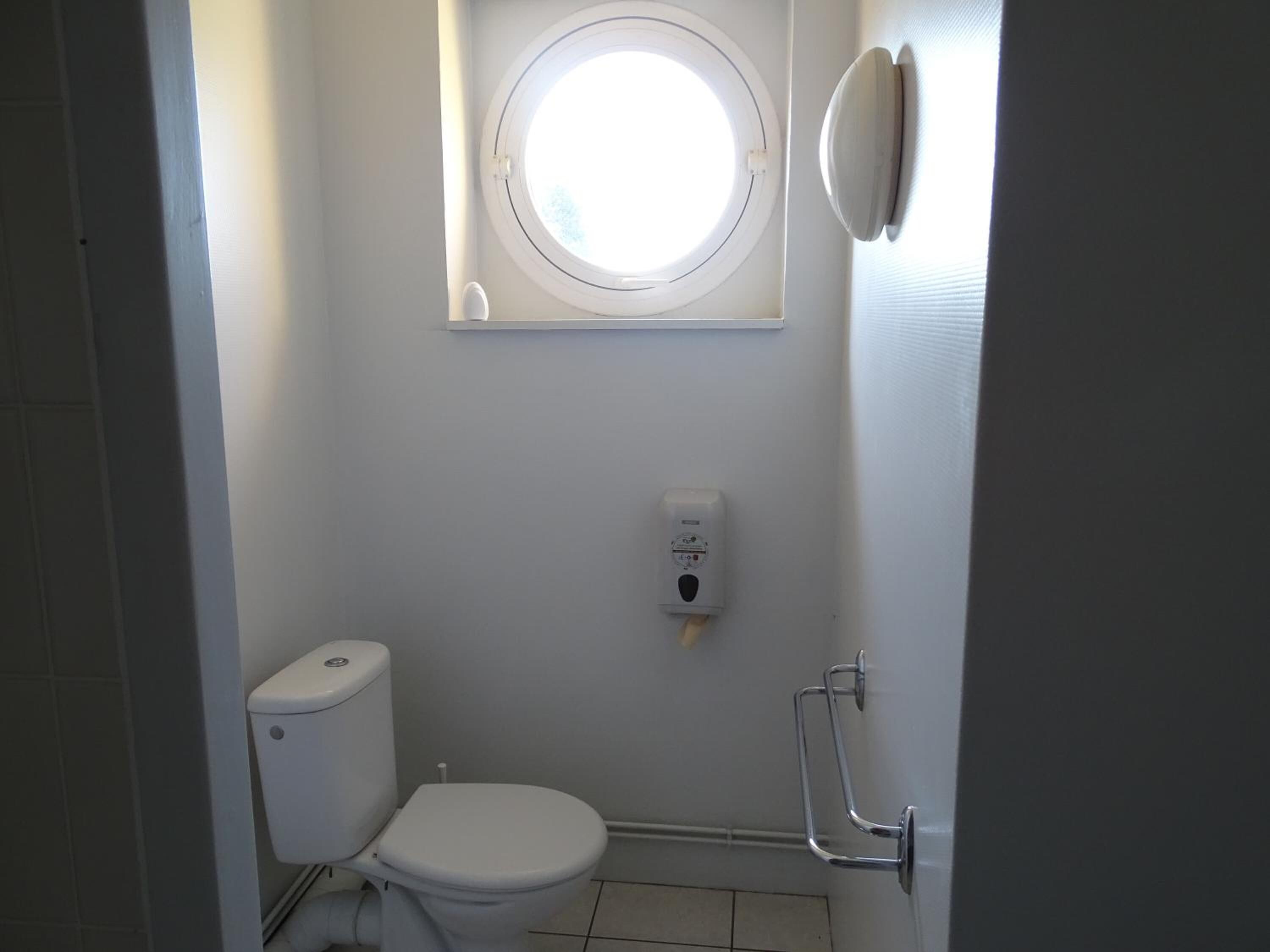 Een kleine, praktische badkamer met toilet, een handdesinfecterend middel en een raam.