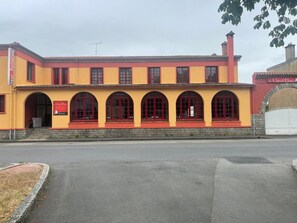 A yellow building with red-framed windows and a stone base. - Hôtel Restaurant Le Cheval Blanc (Cerizay)