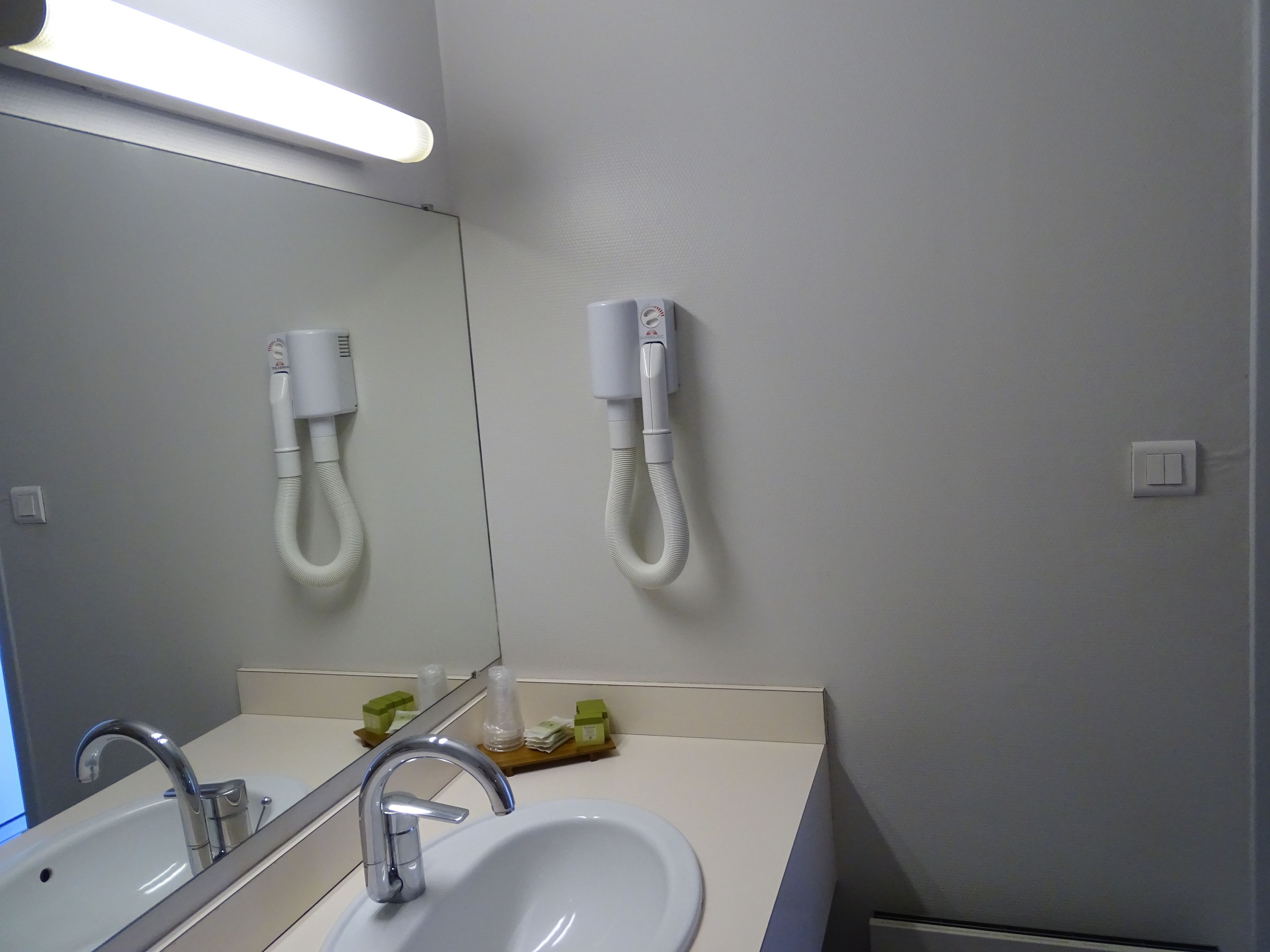 Un baño con lavamanos, espejo y dos secadores de pelo montados en la pared.