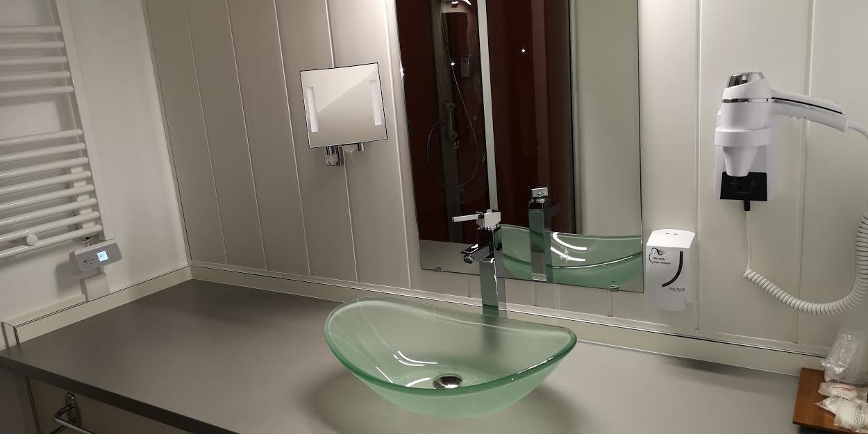 Un baño moderno con un lavabo de cristal, un secador de pelo de mano y un espejo.