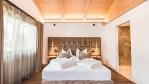 A modern bedroom with a large bed, wooden ceiling beams, and a stone accent wall. - Hotel Weingarten (Appiano Sulla Strada del Vino)