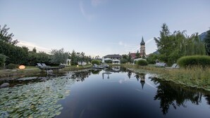 A serene pond with lily pads, lounge chairs, and a gazebo in a landscaped garden. - Hotel Weingarten (Appiano Sulla Strada del Vino)