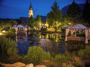 A serene lakeside setting with a gazebo, a pond with lily pads, and a distant church tower.