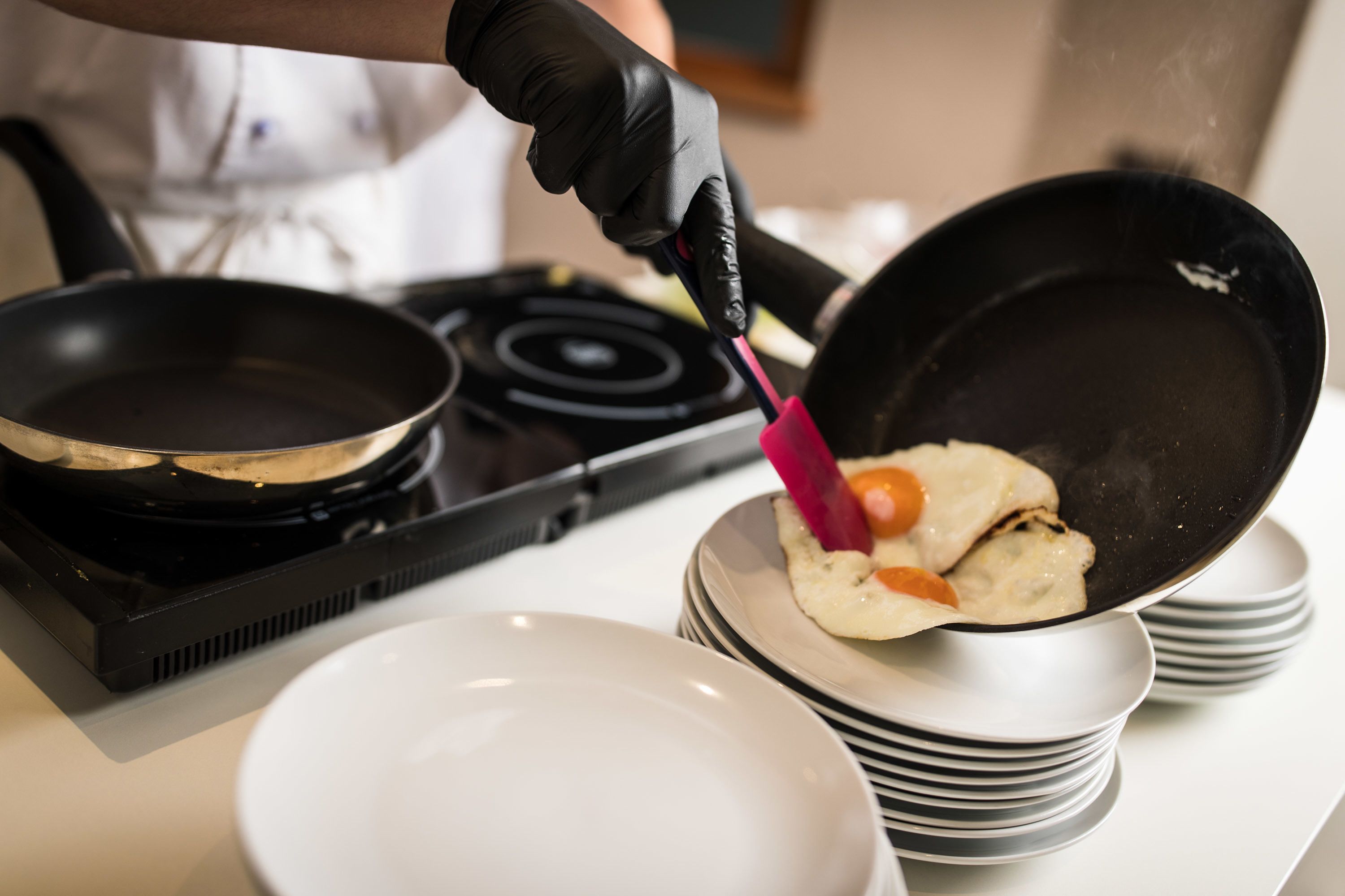 A person cooking with a frying pan on a stove, a stack of plates, and a white bowl.