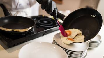 A person cooking with a frying pan on a stove, a stack of plates, and a white bowl.