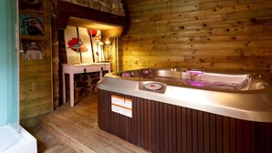 A wooden cabin interior with a hot tub, stone wall, and artwork. - Auberge du Cheval Blanc (Baud)