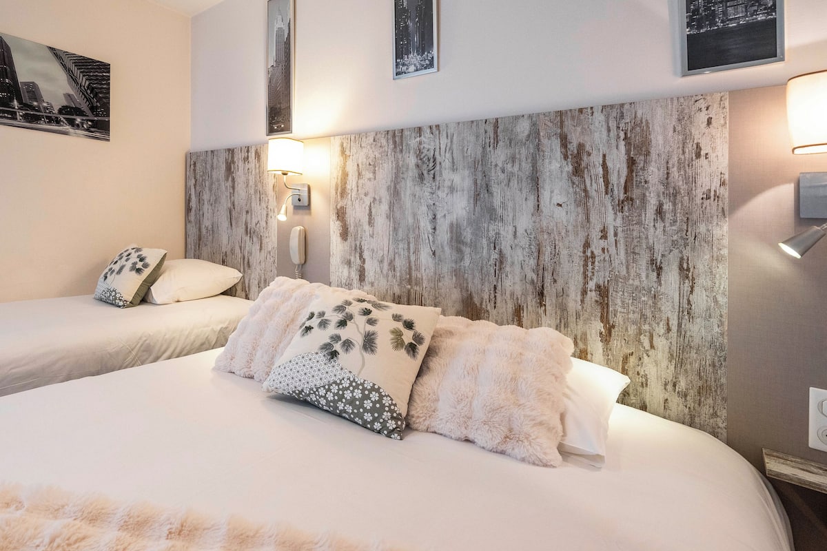 A hotel room with a large bed, two bedside tables, a wall-mounted phone, and a cityscape picture.