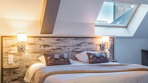 A bedroom with a sloped ceiling, a skylight, and two bedside lamps. - Auberge du Cheval Blanc (Baud)