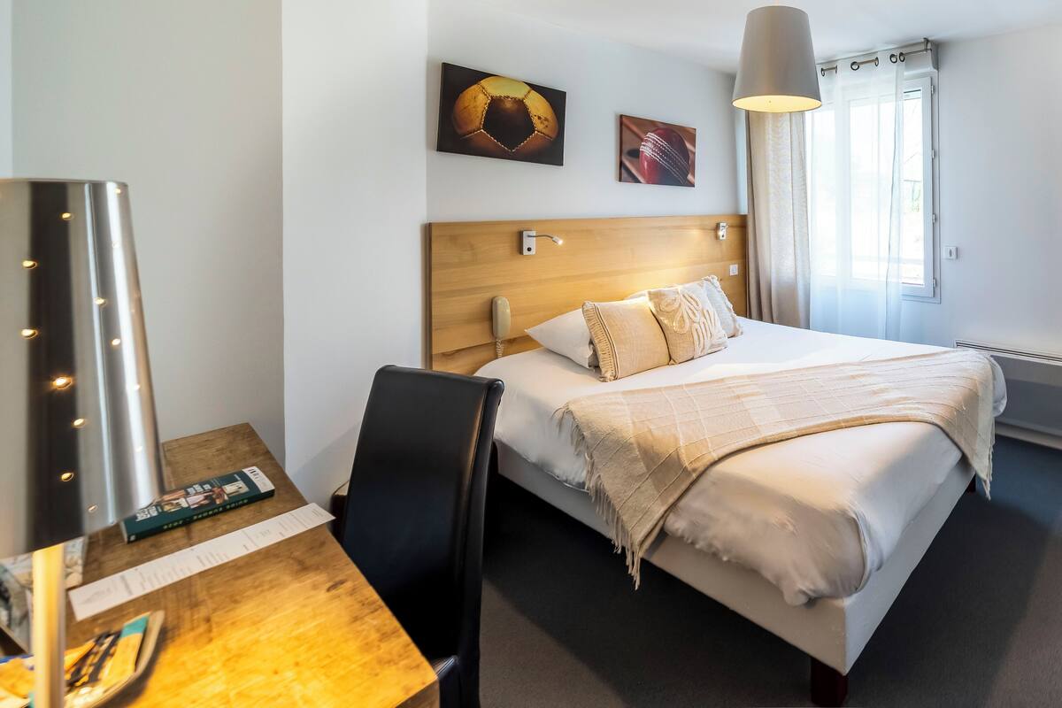 A hotel room with a bed, bedside table, lamp, and artwork on the wall.