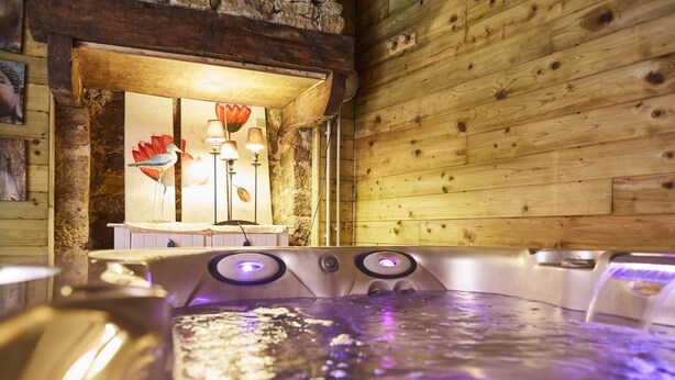 A wooden cabin interior with a hot tub, a stone wall, and a framed artwork. - Auberge du Cheval Blanc (Baud)