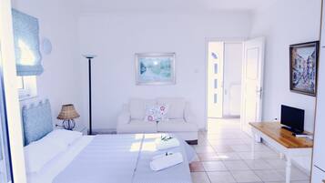 A hotel room with a bed, a sofa, a TV, and a painting on the wall.