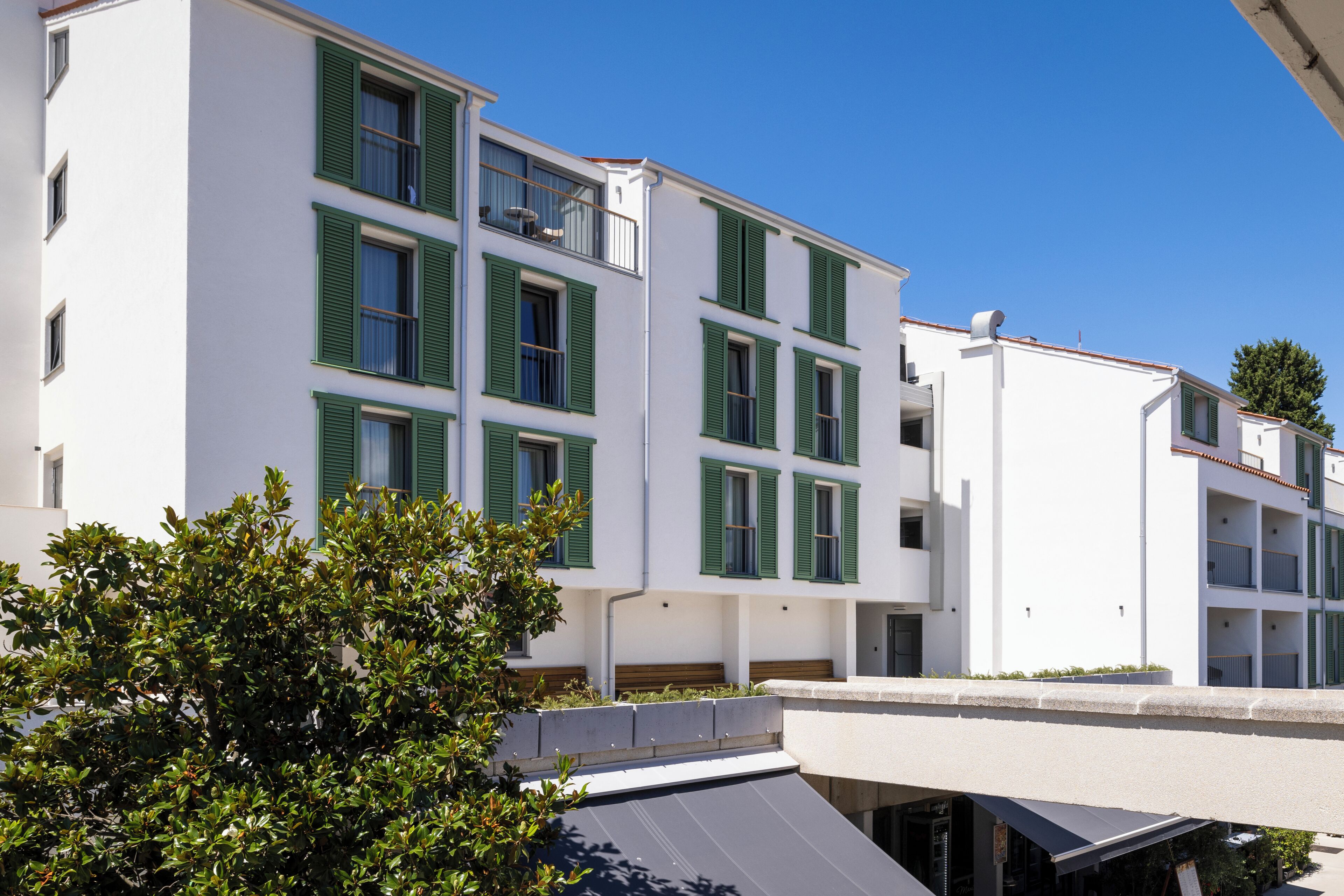 Un immeuble à plusieurs étages, doté d’une façade blanche et de volets verts.