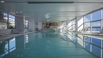 Una piscina interna con pareti di vetro trasparenti, pavimento piastrellato e interni luminosi.