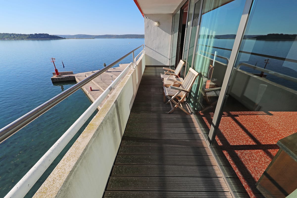 Ein Balkon mit Blick auf einen ruhigen See, Holzstühle und ein rot ausgelegter Bereich.