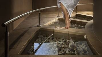 A person sitting on a stone ledge with a pool of water and pebbles below.