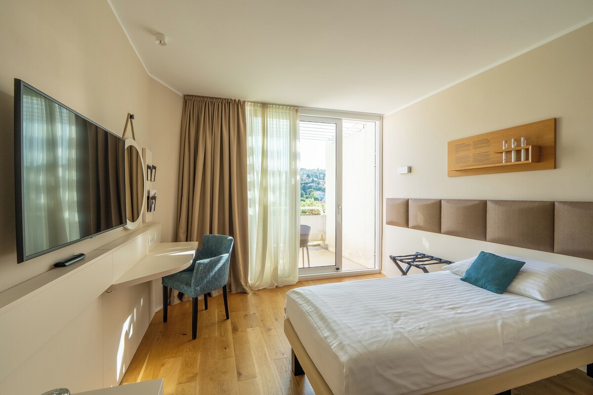 A hotel room with a bed, a desk, a chair, a television, and a sliding glass door leading to an outdoor area.