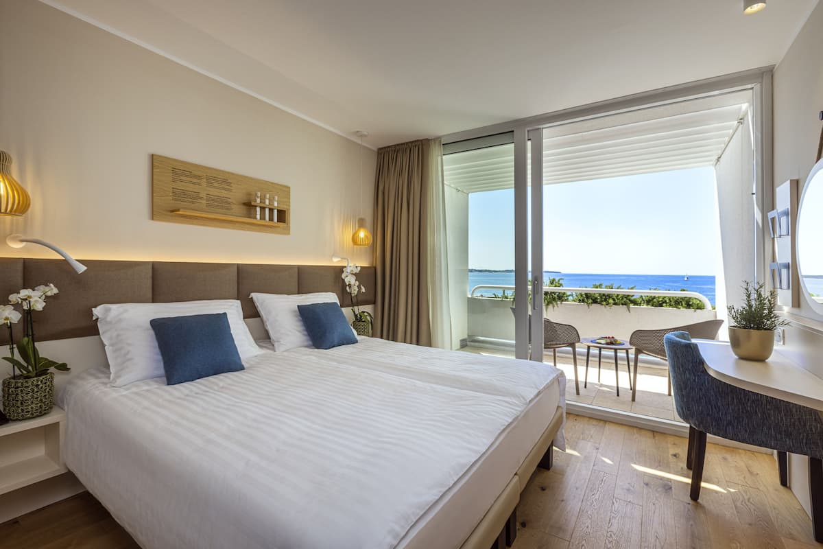 Ein Hotelzimmer mit einem großen Bett, einem Schreibtisch mit Stuhl, Meerblick und einem Balkon mit Sitzgelegenheit.