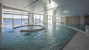 An indoor swimming pool with clear views of the sea through large windows, a circular hot tub, and a poolside area with chairs. - Hotel Histrion - Sava Hotels & Resorts (Piran)
