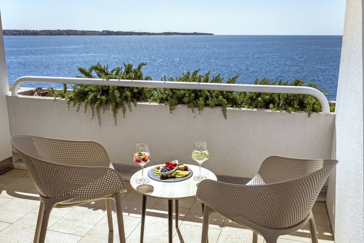 Ein Balkon mit zwei Korbstühlen, einem kleinen runden Tisch und Blick aufs Meer.