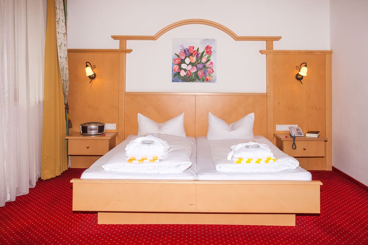Uma cama de casal com lençóis e toalhas brancas, duas mesas de cabeceira com luminárias, uma cabeceira de madeira e um quadro com flores na parede.