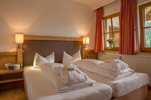 Un lit double avec du linge de lit blanc, une tête de lit en bois, des tables de chevet avec des lampes et une fenêtre avec des rideaux.