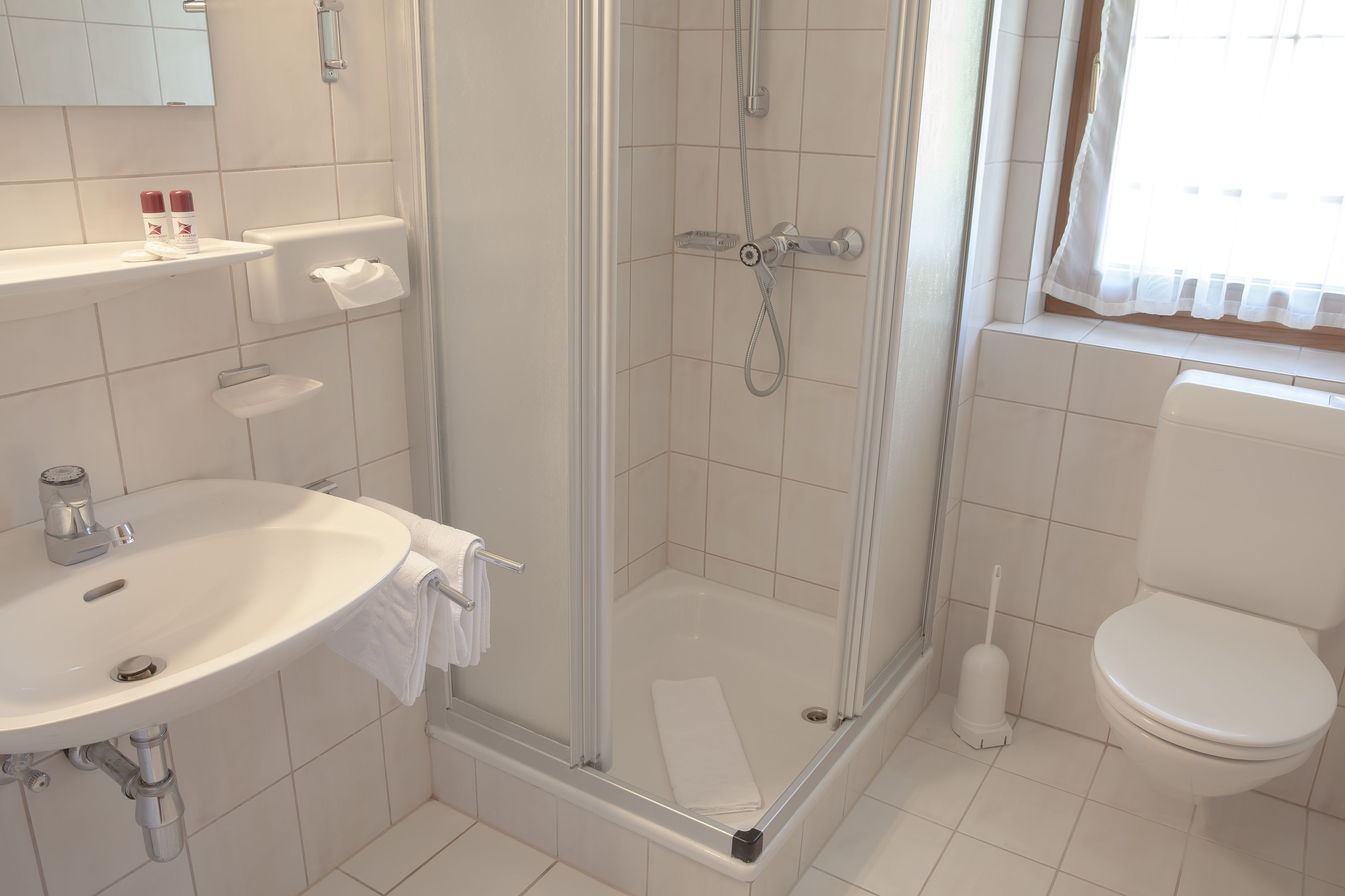 Un baño con ducha, inodoro, lavamanos y ventana con cortinas.