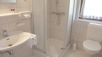 Un baño con ducha, inodoro, lavamanos y ventana con cortinas.