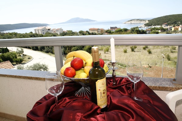 Un balcón con una mesa dispuesta para dos personas, que incluye una botella de vino, dos copas y un bol de fruta.