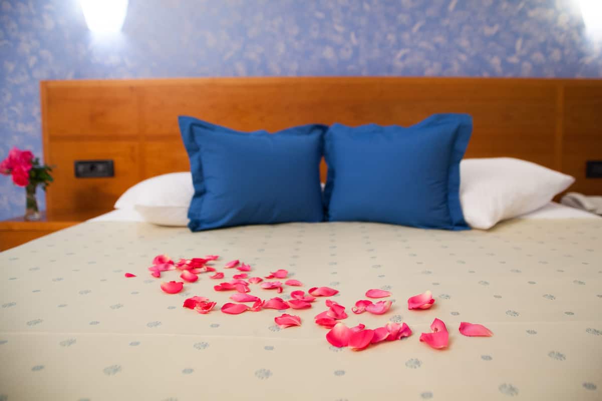 Ein Bett mit blauen und weißen Kissen, einer betttdecke mit Blumenmuster und verstreuten Rosenblättern.