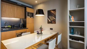 A modern kitchen with wooden cabinets, a Bosch microwave, a black hanging light, and a white dining table with chairs.