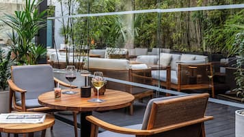 An outdoor seating area with wooden furniture and glass tables, surrounded by lush greenery.