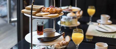 Un bufé de desayuno con diversas pastas, frutas y bebidas en mesas escalonadas.