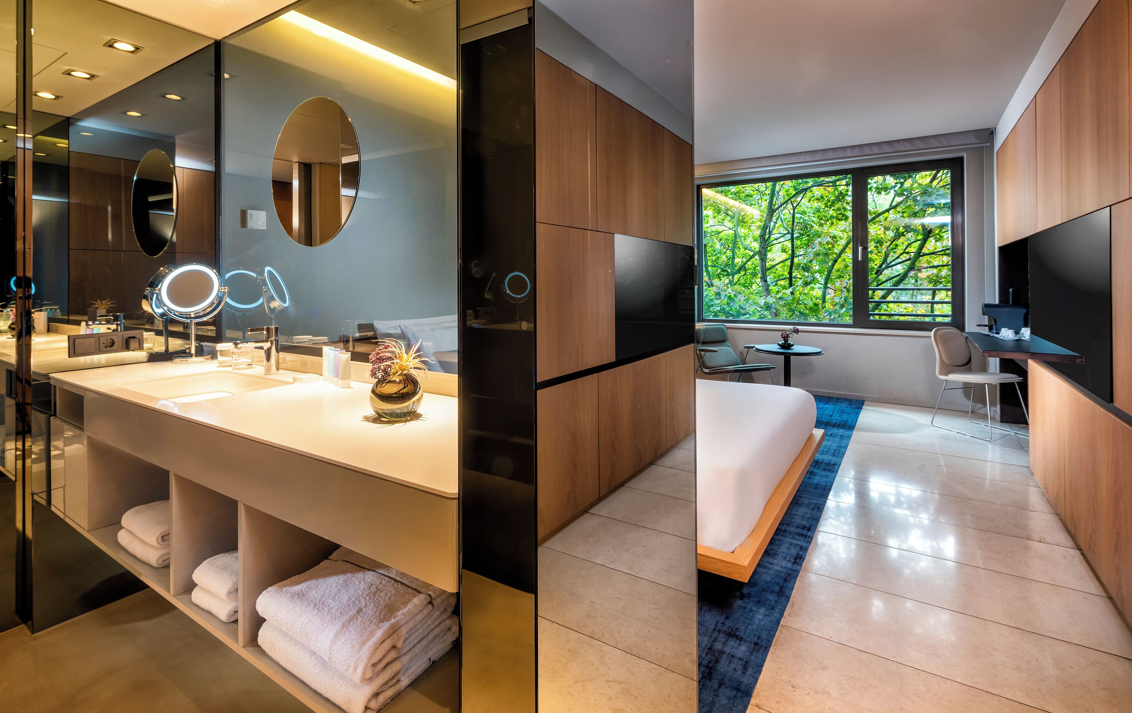Una habitación de hotel moderna con un espejo grande, tocador y una cama con un tapete azul decorativo.
